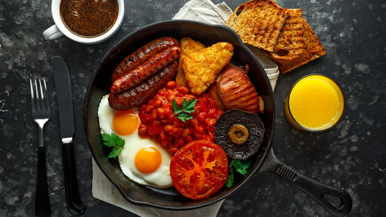 A full English breakfast in a pan: sausages, bacon, a hash brown, beans, fried eggs, tomato and mushroom, with toast